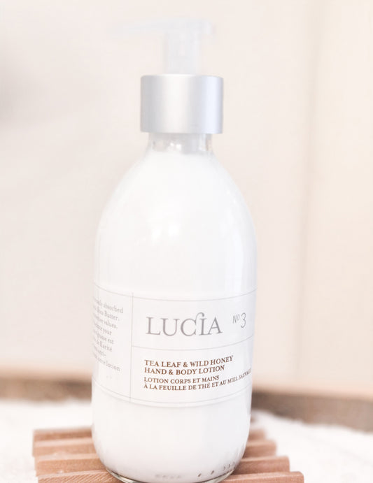Lucá tea leaf and wild honey hand and body lotion bottle on a wooden surface with a neutral background