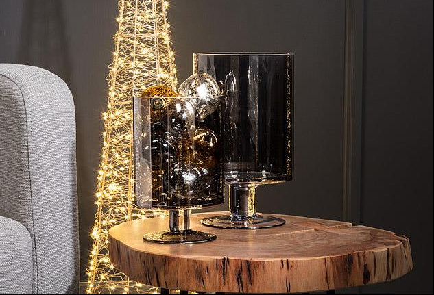 Decorative table with a small Christmas tree and glassware against a dark wall.