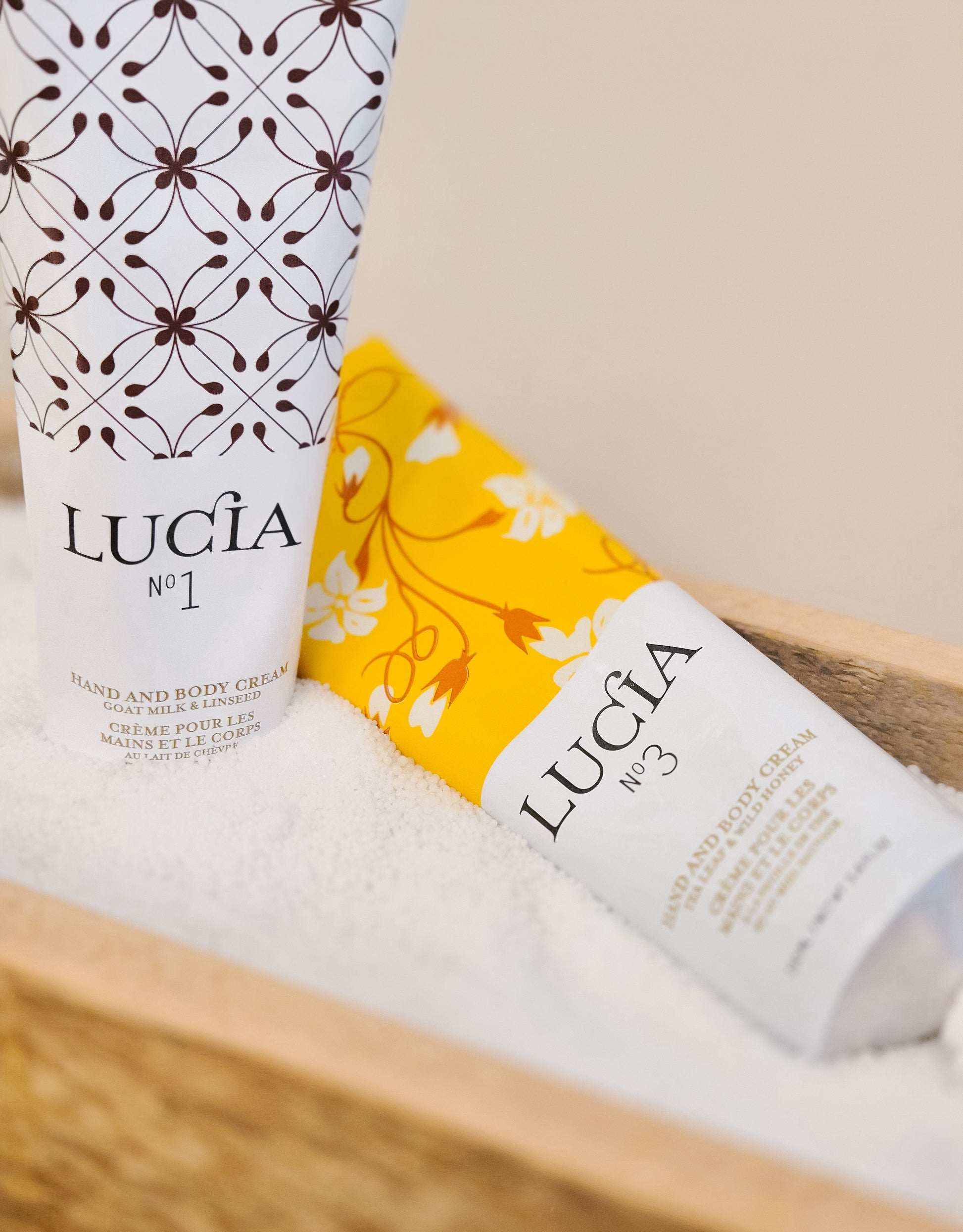 Two bottles of Lucia hand and body cream on a wooden surface with a neutral background.