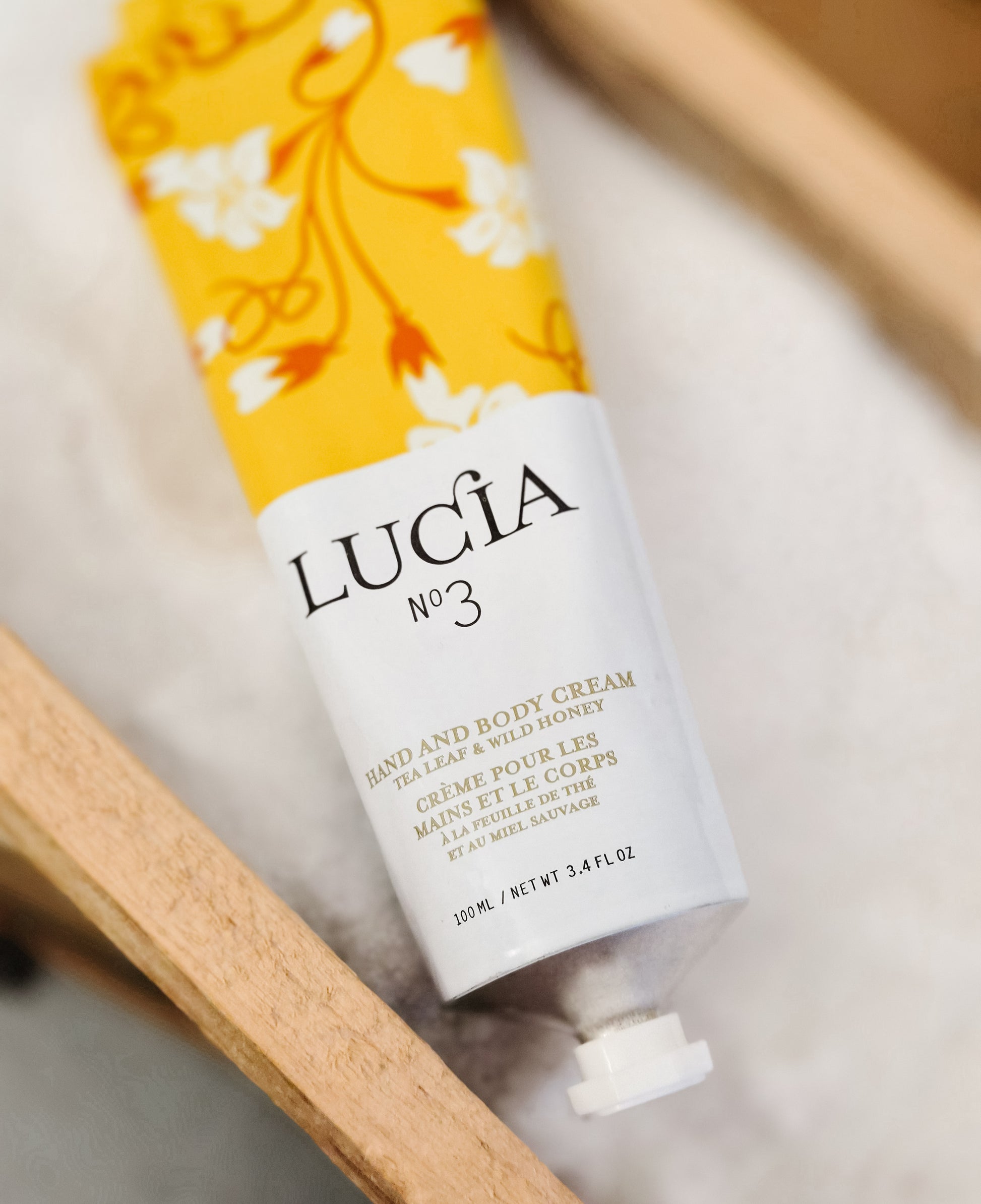 Tube of Lucia No. 3 hand and body cream with a floral design on a wooden surface.