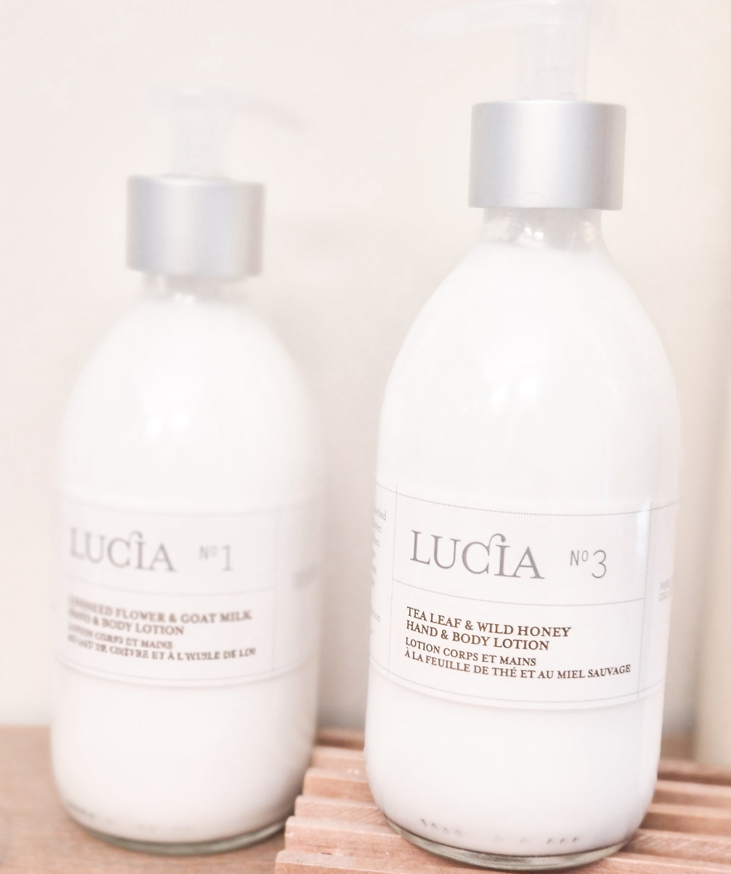 Two bottles of Lucia hand and body lotion on a wooden surface with a light background