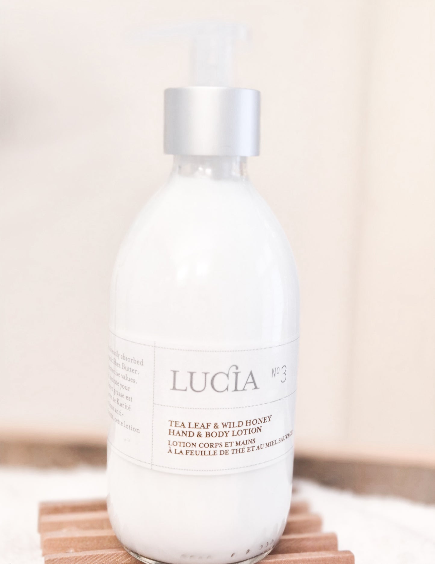 Lucá tea leaf and wild honey hand and body lotion bottle on a wooden surface with a neutral background