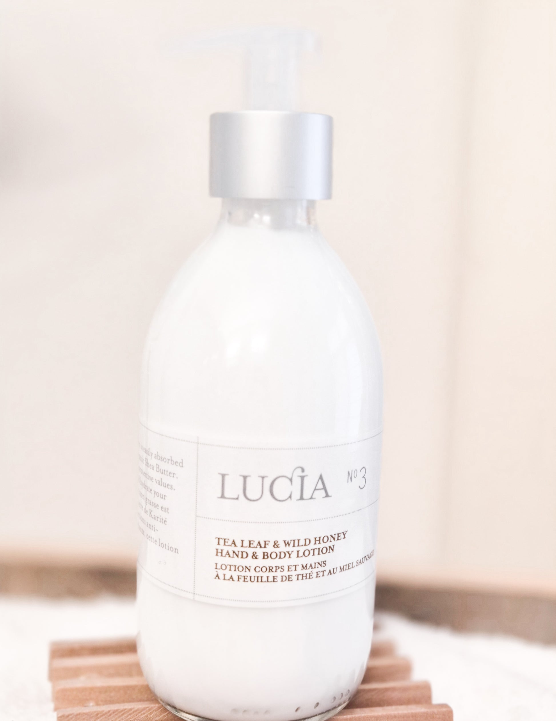 Lucá tea leaf and wild honey hand and body lotion bottle on a wooden surface with a neutral background