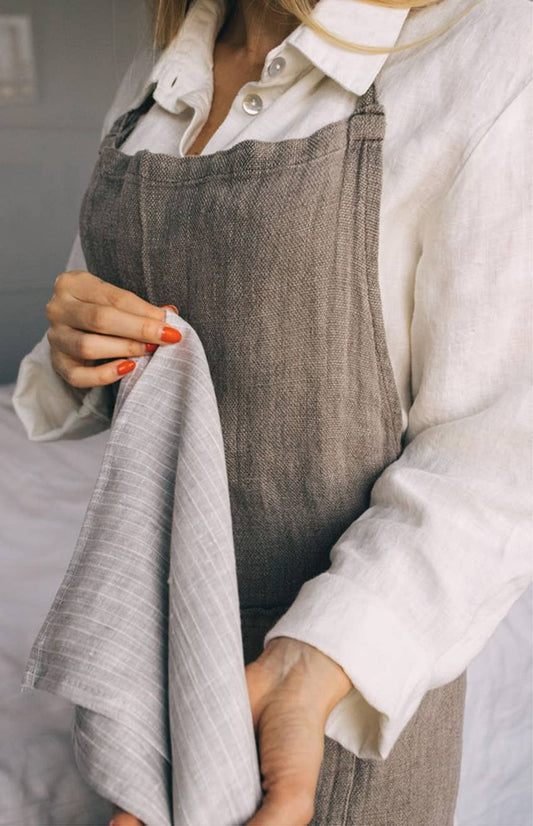 Person wearing a white shirt and gray apron holding a white towel.